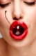A closeup of a young pretty women face holding a yummy cherry in her mouth.
